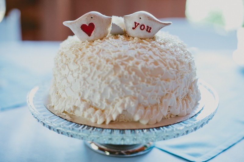 Small wedding cake with cornelli lace piping, topped with two white and red birds, on a vintage cake plate. 