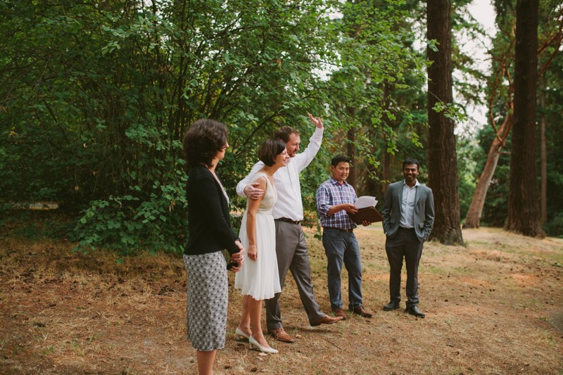 Groom waves at guests at small outdoor wedding. 