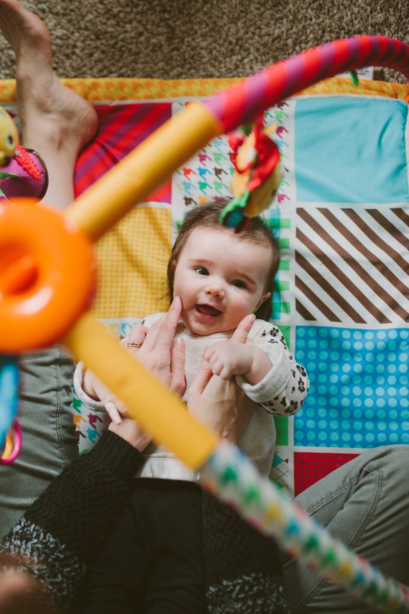 Mama squishing adorable baby's cheeks, while baby lays on a colorful play mat. 