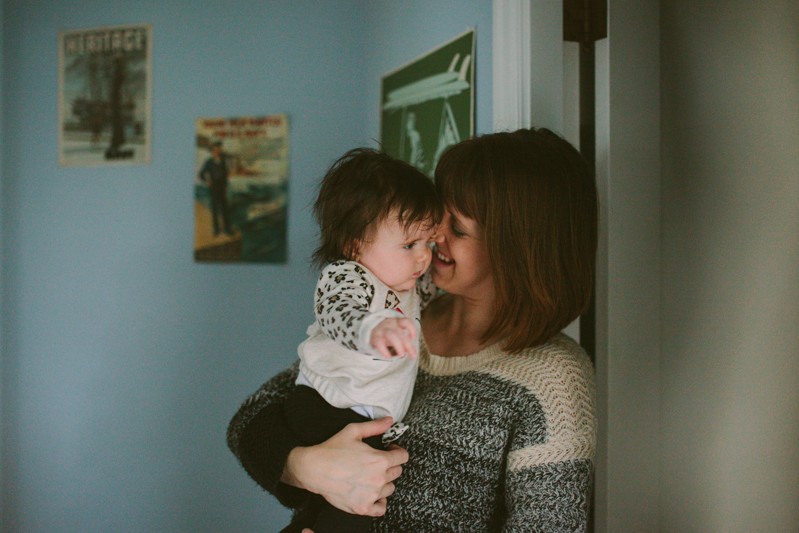A young mom smiles while holding her baby girl, at their in-home portrait session, in Kitsap County, WA. 