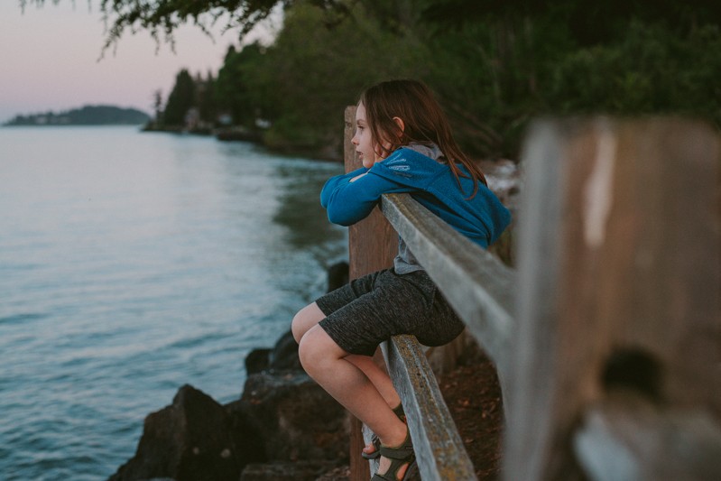 Little boy sitting on a fence, watching the ferry sail by on Bainbridge Island, WA.