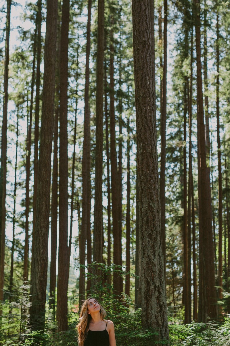 Model looks up at tall tress in forest, at Kitsap Memorial State Park.