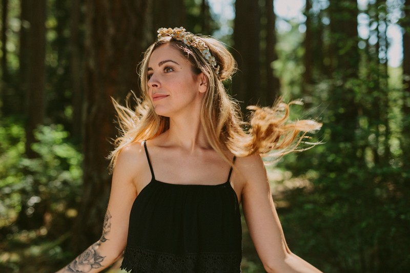 Model with long hair and faux flower crown dances in forest.