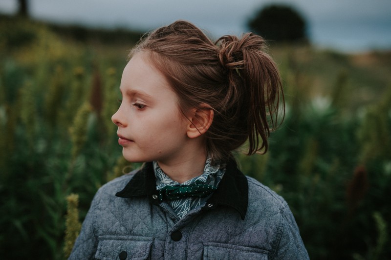 Little boy with long hair, up in a hair tie, wearing a collard shirt and polka dot bow tie, in Port Townsend, WA.