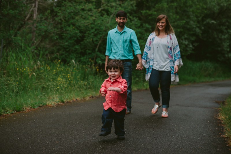 Cute toddler runs, with couple holding hands and walking behind him.