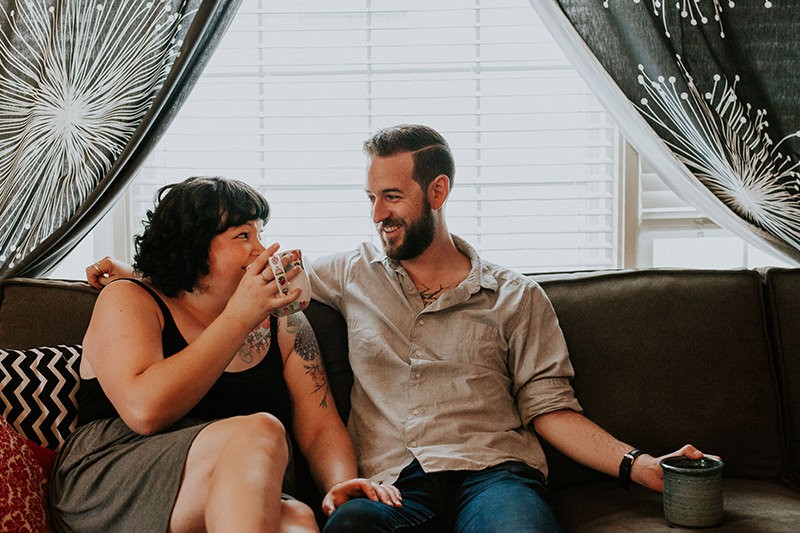 Modern couple sipping coffee on their couch, with starburst curtains in the background.
