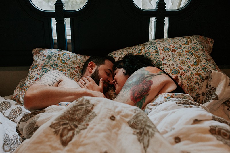 Intimate portraits, with cute tattooed couple laying in bed and cuddling.