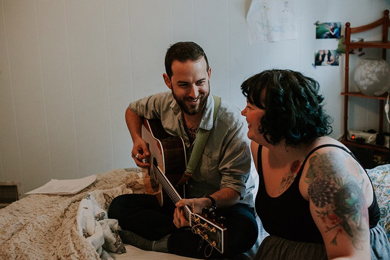 Sweet tattooed couple singing and playing guitar, at home, in Bremerton, WA.